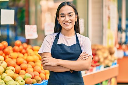 Young latin shopkeeper girl with arms crossed smiling happy at t